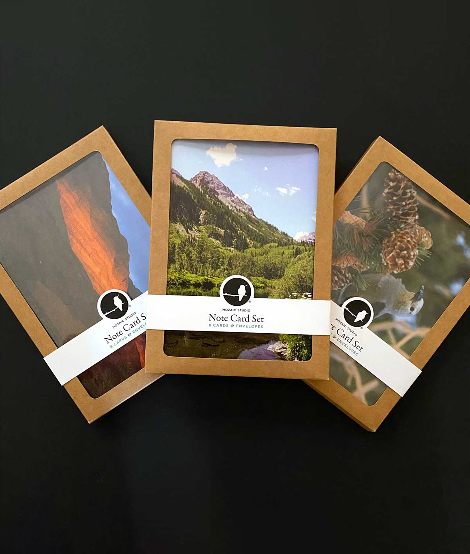 Three boxes of Mozaic Studio note card sets in recycled paper packaging, showcasing a variety of designs.