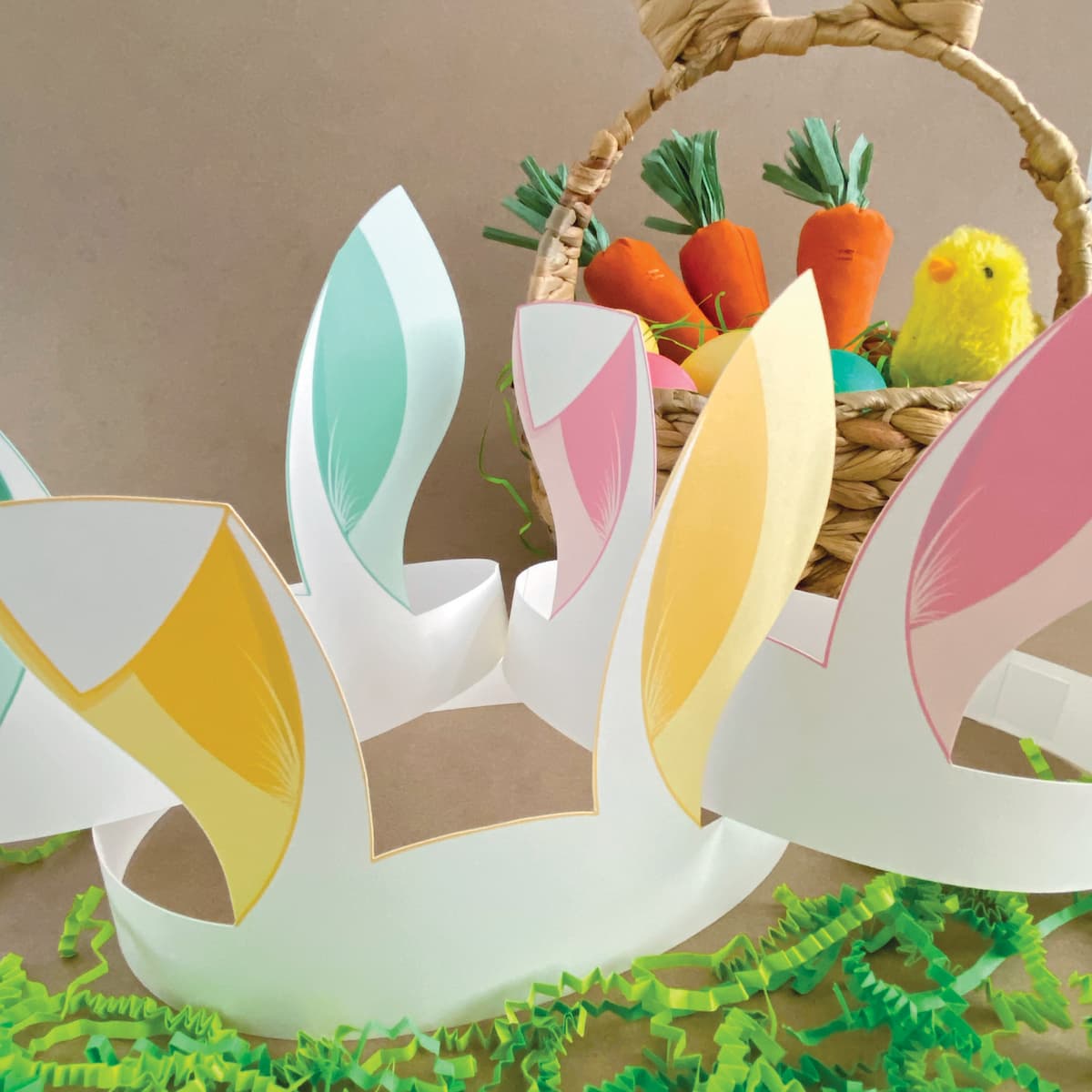 Group of three Easter bunny crowns in pastel yellow, pink, green with Easter props