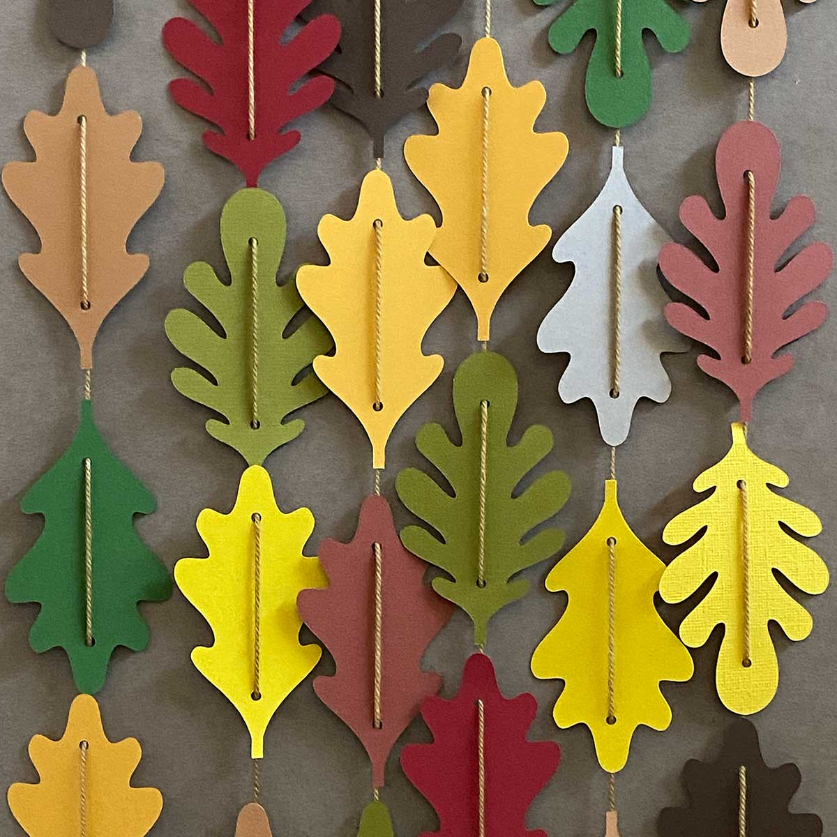 Paper leaves in fall colors strung together in vertical garlands for CakewalkDIY.