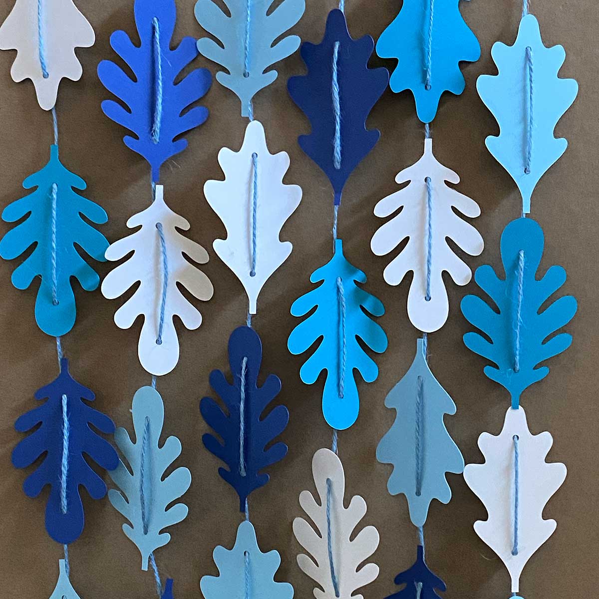 Paper leaves in shades of blue strung together in vertical garlands for CakewalkDIY.
