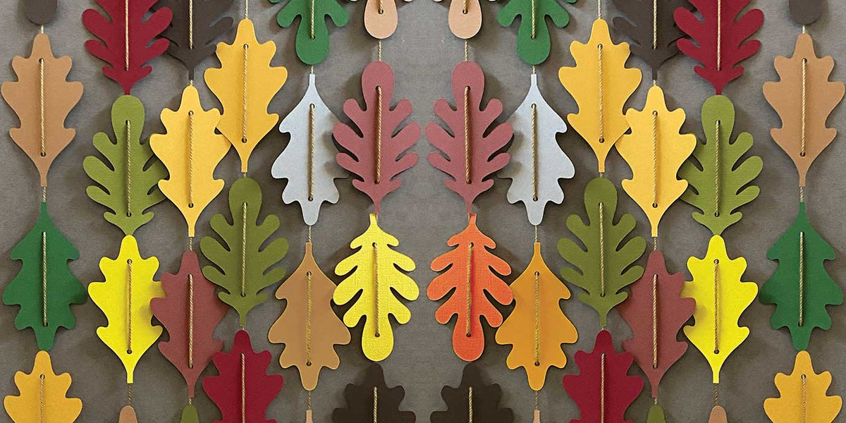 Paper leaves in fall colors strung together on tan yard to showcase a leaf garland for CakewalkDIY.