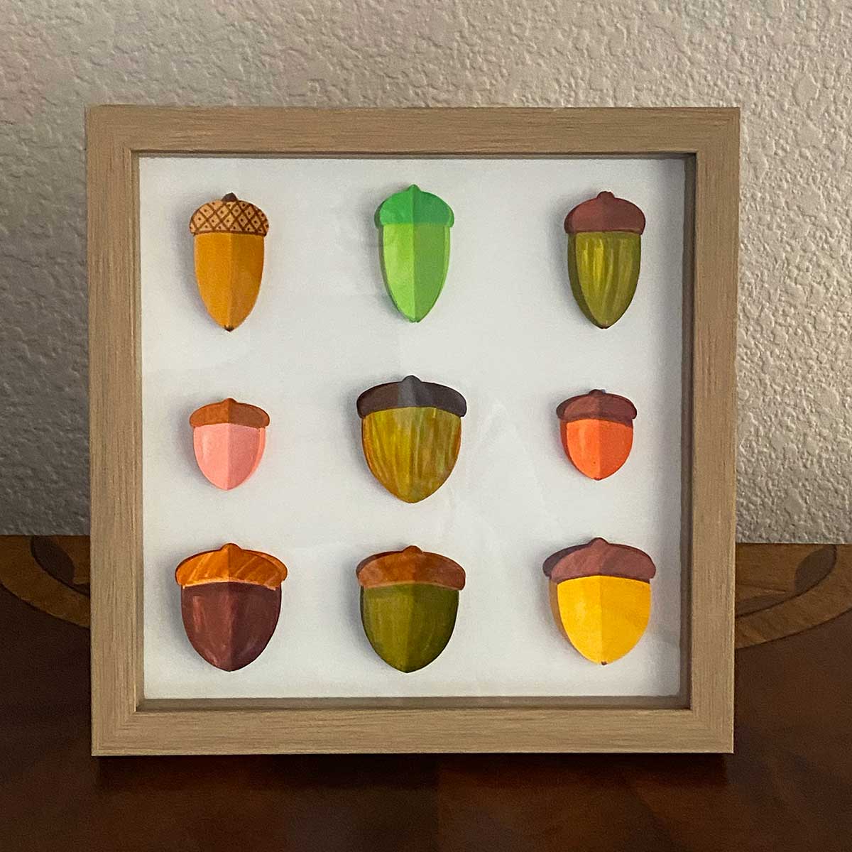 Square shadow box frame with 9 colorful 3D paper acorns to showcase     a Cakewalk DIY Paper Craft tutorial.