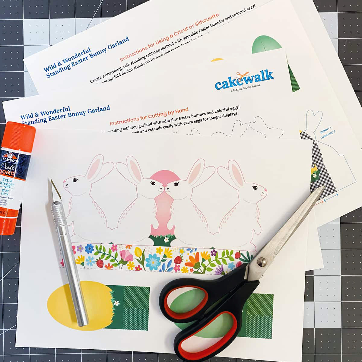 Crafting materials including paper with bunny designs, glue stick, pen, and scissors on a cutting mat with Cakewalk branding.