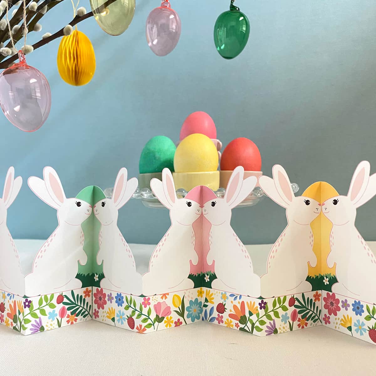 Finished printable standing bunny garland displayed on Easter table with basket, grass, colored eggs, and jelly beans – self-standing accordion fold tabletop decor